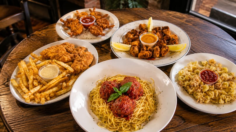 Table laden with plates of spaghetti and meatballs, fried chicken, calamari, and popcorn shrimp.